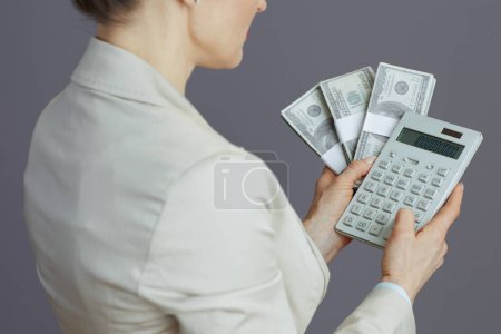 Photo for Closeup on woman worker in a light business suit with calculator and dollars money packs against grey background. - Royalty Free Image