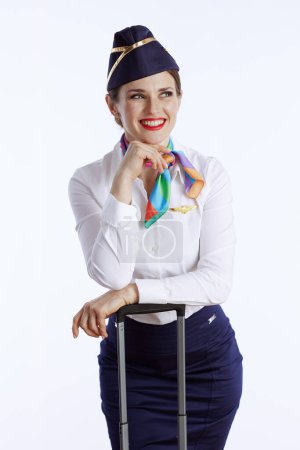 Foto de Sonriente elegante azafata femenina sobre fondo blanco en uniforme con bolsa de viaje mirando a un lado. - Imagen libre de derechos