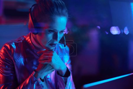 Photo for Neon metaverse futuristic concept. pensive elegant female with laptop and headset talking video call in modern office. - Royalty Free Image