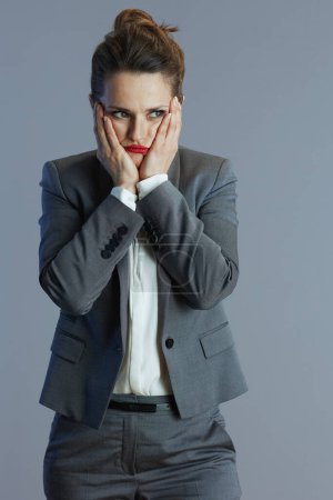 Téléchargez les photos : Stressé femme d'affaires à la mode en costume gris isolé sur gris. - en image libre de droit