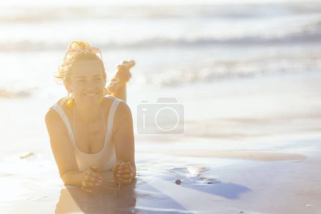 Foto de Mujer elegante feliz en traje de baño blanco que pone en la playa. - Imagen libre de derechos