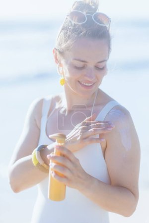 Foto de Mujer de mediana edad elegante feliz en traje de baño blanco en la playa usando spf. - Imagen libre de derechos