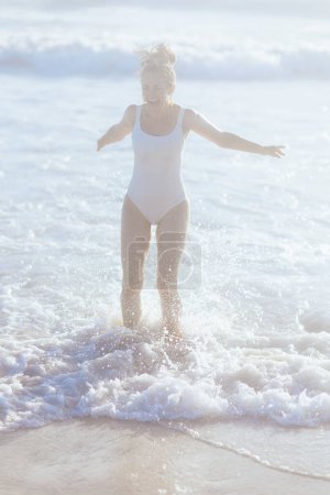 Foto de Retrato de larga duración de la mujer de mediana edad moderna feliz en ropa de playa blanca en la playa que se divierte. - Imagen libre de derechos