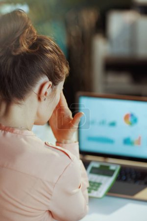 Téléchargez les photos : Vu de derrière femme moderne avec calculatrice et ordinateur portable dans le bureau moderne. - en image libre de droit