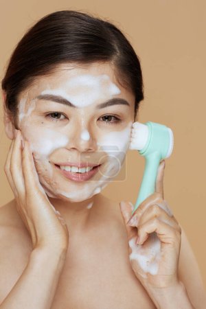 Téléchargez les photos : Jeune femme avec masseur lavage visage sur fond beige. - en image libre de droit