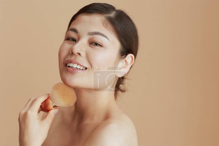 Téléchargez les photos : Portrait de jeune femme avec brosse de maquillage isolée sur fond beige. - en image libre de droit