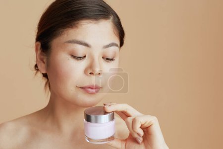 Foto de Moderna mujer asiática con crema facial tarro en fondo beige. - Imagen libre de derechos