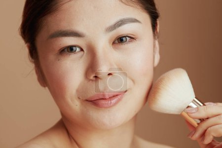 Foto de Retrato de mujer asiática moderna con cepillo de maquillaje sobre fondo beige. - Imagen libre de derechos