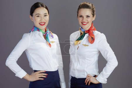 Photo for Happy stylish female stewardesses in blue skirt, white shirt and scarf isolated on gray. - Royalty Free Image