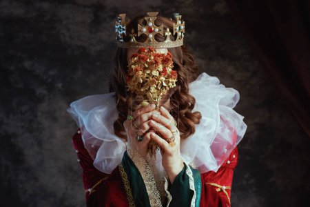 Photo for Closeup on medieval queen in red dress with dried flower, white collar and crown on dark gray background. - Royalty Free Image