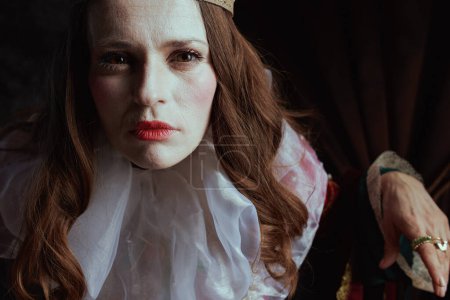 Foto de Aterradora reina medieval en vestido rojo con cuello blanco sobre fondo gris oscuro. - Imagen libre de derechos
