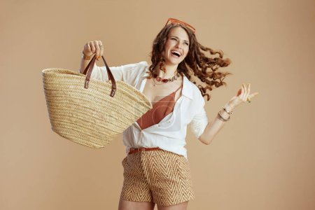 Foto de Vacaciones en playa. mujer con estilo feliz en blusa blanca y pantalones cortos aislados en fondo beige con bolsa de paja y gafas de sol. - Imagen libre de derechos