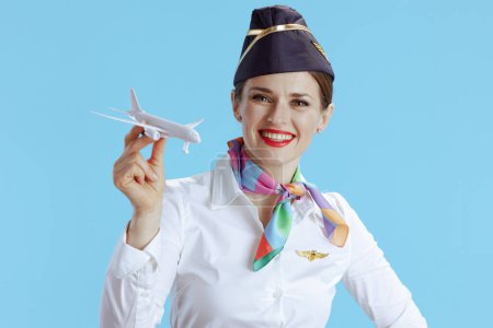 Téléchargez les photos : Heureuse hôtesse de l'air moderne femme sur fond bleu en uniforme avec un petit avion. - en image libre de droit
