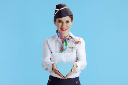 Foto de Feliz mujer moderna azafata sobre fondo azul en uniforme mostrando el corazón. - Imagen libre de derechos