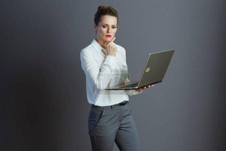 Téléchargez les photos : Chère jeune femme travailleur en chemisier blanc en utilisant ordinateur portable isolé sur gris. - en image libre de droit