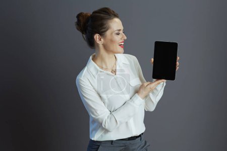 Téléchargez les photos : Souriant élégant femme travailleur en chemisier blanc montrant tablette PC écran vide isolé sur fond gris. - en image libre de droit