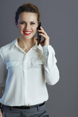 Photo for Happy 40 years old small business owner woman in white blouse using a mobile phone isolated on grey background. - Royalty Free Image