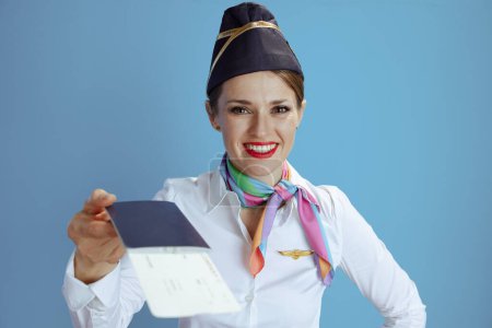 Foto de Sonriente azafata femenina con estilo aislado sobre fondo azul en uniforme con billetes de avión y pasaporte. - Imagen libre de derechos
