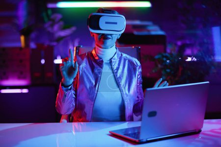 Téléchargez les photos : Neon metaverse concept futuriste. femme moderne de 40 ans en réalité virtuelle lunettes dans le bureau moderne travaillant en réalité virtuelle. - en image libre de droit