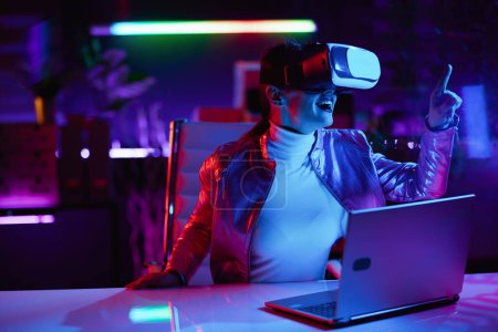 Photo for Neon metaverse futuristic concept. excited elegant woman in vr headset in modern office working in virtual reality. - Royalty Free Image