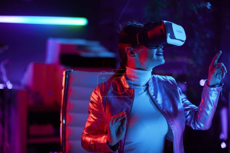 Téléchargez les photos : Neon metaverse concept futuriste. curieuse femme moderne dans vr casque conception réalité virtuelle dans le bureau moderne. - en image libre de droit