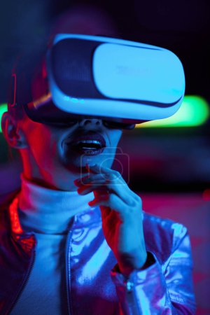 Foto de Concepto futurista neón metaverso. mujer con estilo excitado en gafas de realidad virtual sobre fondo oscuro. - Imagen libre de derechos