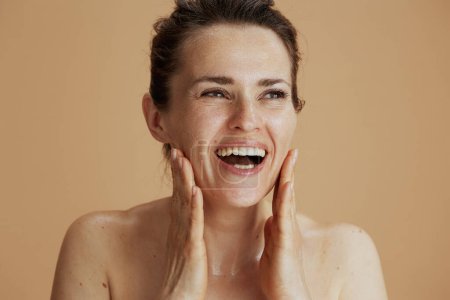 Foto de Sonriente joven con la cara mojada lavando sobre fondo beige. - Imagen libre de derechos