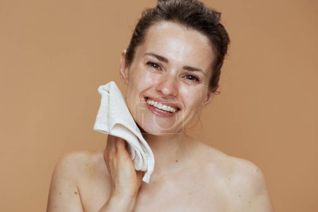 Téléchargez les photos : Femme moderne souriante avec le visage de lavage de serviette sur fond beige. - en image libre de droit