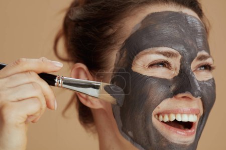 Téléchargez les photos : Heureuse jeune femme avec brosse et masque cosmétique isolé sur beige. - en image libre de droit