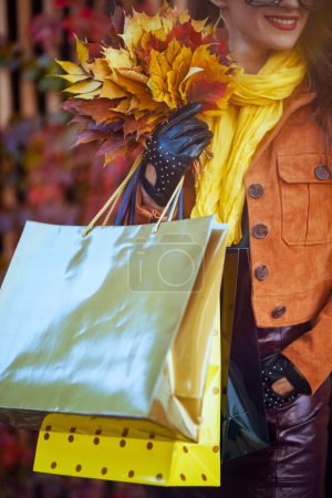 Photo for Hello october. smiling 40 years old woman in orange trench coat with shopping bags and autumn yellow leaves in the city. - Royalty Free Image