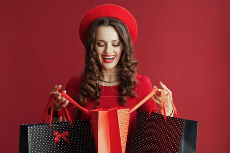 Téléchargez les photos : Joyeux Valentin. heureux élégant femme d'âge moyen en robe rouge et béret sur fond rouge avec des sacs à provisions. - en image libre de droit