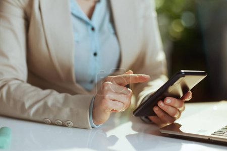 Téléchargez les photos : Gros plan sur comptable femme dans un costume d'affaires léger dans le bureau vert en utilisant smartphone. - en image libre de droit