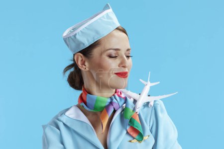 Photo for Elegant female air hostess on blue background in blue uniform with a little airplane. - Royalty Free Image