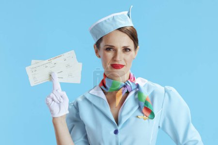 Photo for Elegant female stewardess isolated on blue background in blue uniform with flight tickets. - Royalty Free Image