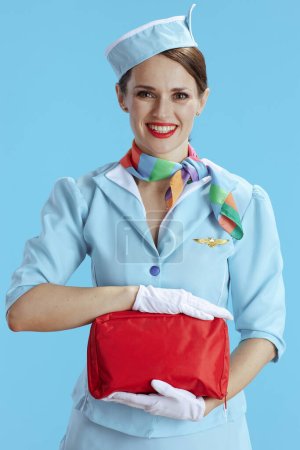 Photo for Smiling elegant female flight attendant against blue background in blue uniform with first aid kit. - Royalty Free Image