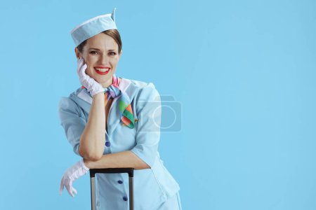Foto de Anfitriona de aire femenino elegante feliz contra fondo azul en uniforme azul con bolsa de carro. - Imagen libre de derechos