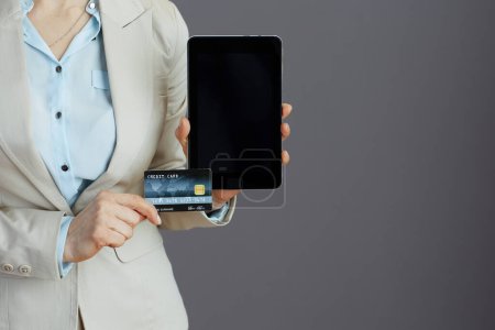 Photo for Closeup on woman employee in a light business suit with credit card using applications on tablet PC isolated on gray background. - Royalty Free Image