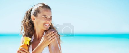 Téléchargez les photos : Jeune femme sur la plage appliquant crème solaire et regardant sur l'espace de copie - en image libre de droit