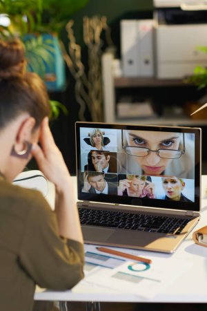 Téléchargez les photos : Vu de derrière femme moderne avec ordinateur portable ayant webcam réunion dans le bureau moderne. - en image libre de droit