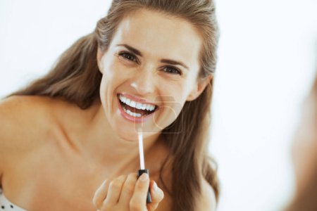 Téléchargez les photos : Happy jeune femme appliquant gloss lèvre dans la salle de bain - en image libre de droit