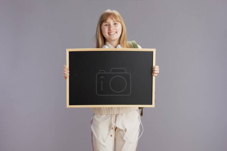 Téléchargez les photos : Adolescent moderne souriant fille en survêtement beige montrant tableau blanc contre gris. - en image libre de droit