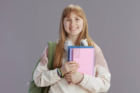 Foto de Retrato de adolescente feliz de moda en chándal beige con mochila, cuadernos y auriculares aislados en gris. - Imagen libre de derechos