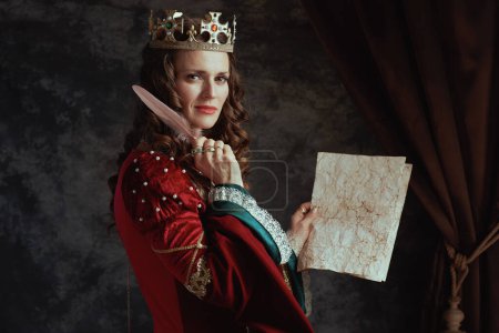 Foto de Reina medieval en vestido rojo con pergamino y corona sobre fondo gris oscuro. - Imagen libre de derechos