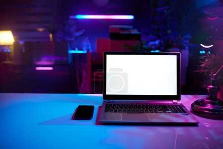 Foto de Neon metaverse futuristic concept. modern office with desk and laptop blank screen. - Imagen libre de derechos
