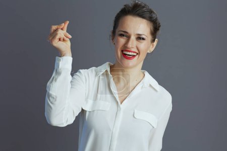 Foto de Feliz mujer propietaria de la pequeña empresa de moda en blanco blusa dedos haciendo clic aislado sobre fondo gris. - Imagen libre de derechos