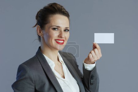 Téléchargez les photos : Souriant élégant d'âge moyen propriétaire de petite entreprise femme en costume gris avec carte de visite isolé sur fond gris. - en image libre de droit