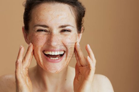 Foto de Retrato de mujer moderna sonriente con exfoliante facial aislado sobre fondo beige. - Imagen libre de derechos