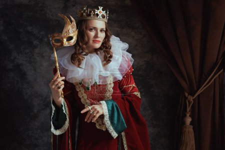 Photo for Medieval queen in red dress with venetian mask, white collar and crown on dark gray background. - Royalty Free Image