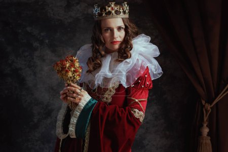 Photo for Medieval queen in red dress with dried flower, white collar and crown on dark gray background. - Royalty Free Image