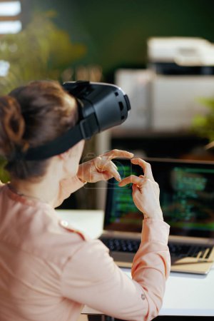 Photo for Seen from behind modern business woman with laptop and virtual reality glasses in modern office showing heart shaped hands. - Royalty Free Image